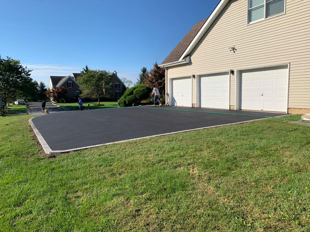 Wide asphalt parking pad with stone border at a three-car garage