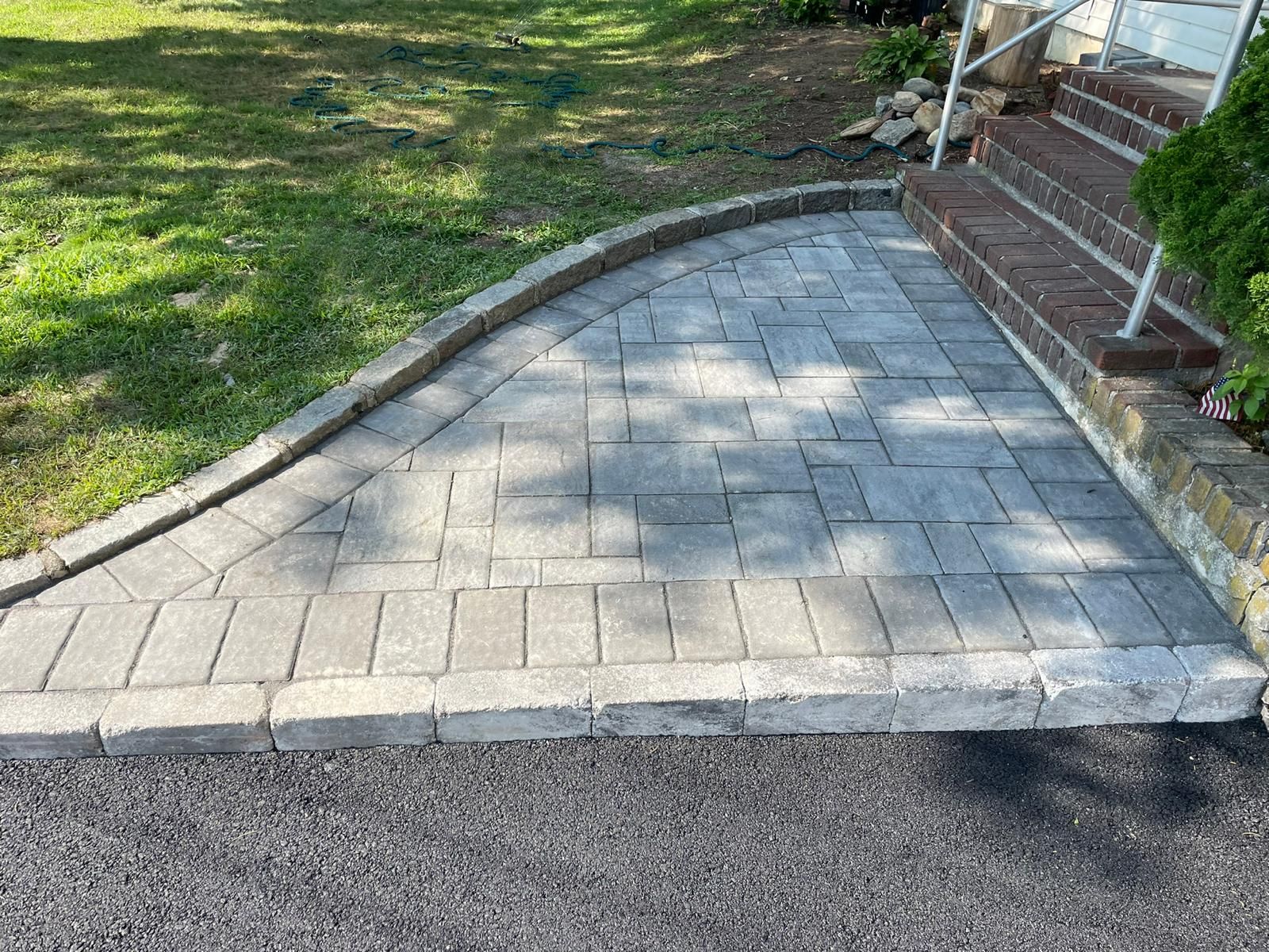 Gray paver landing with cobblestone border beside brick steps and asphalt drive