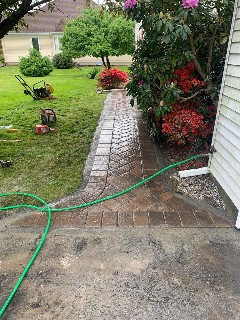 Brick paver walkway with dark border curving along the side of a home