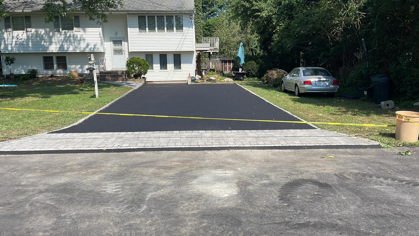 Long asphalt driveway with a gray paver apron at the street
