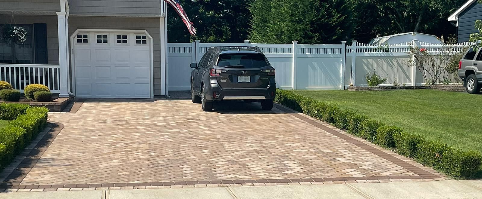 Tan paver driveway with brick border and manicured hedges