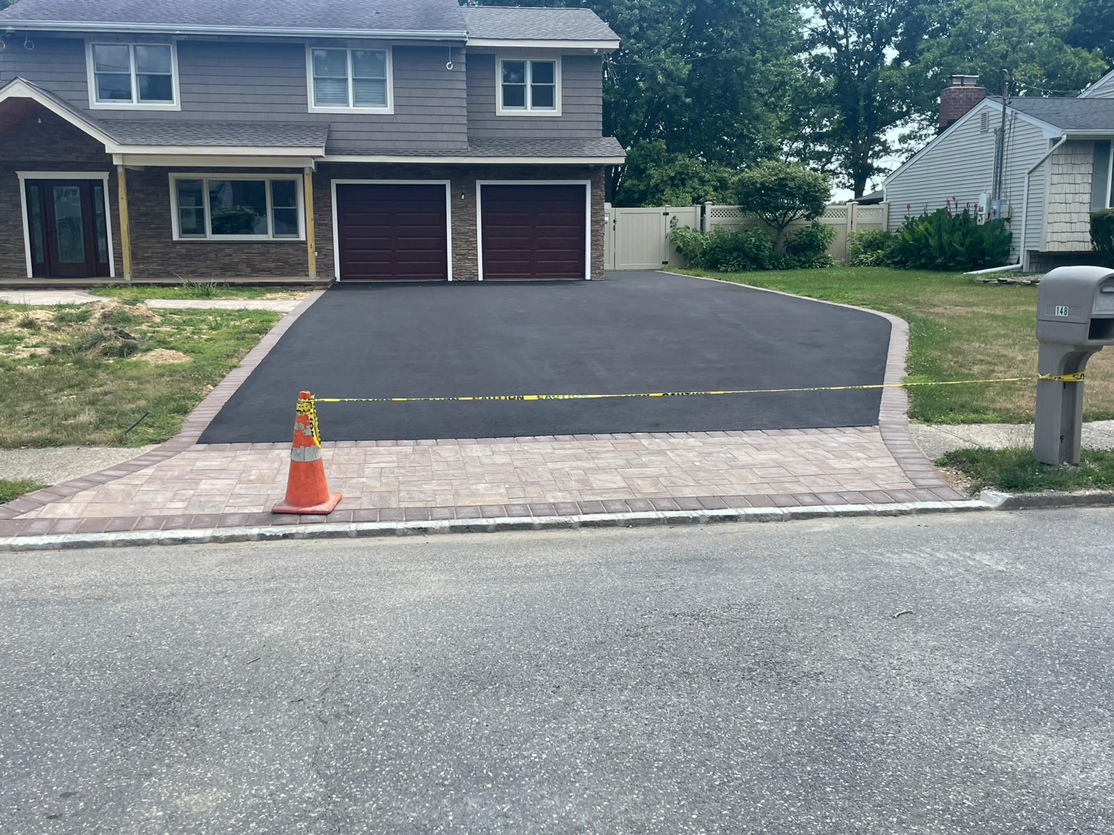 New asphalt driveway with an earth-tone paver apron at the curb