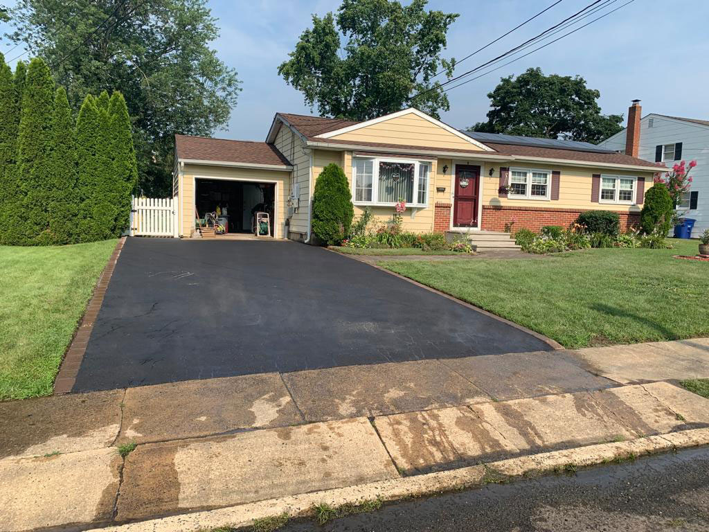 Resurfaced asphalt driveway with brick paver edging at a ranch home